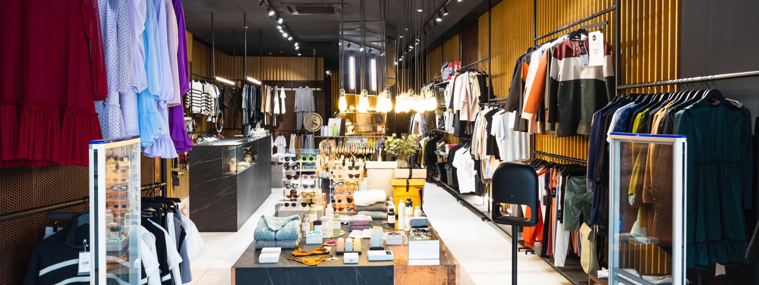 The interior of a clothing store with fashionable clothes hanging on racks.